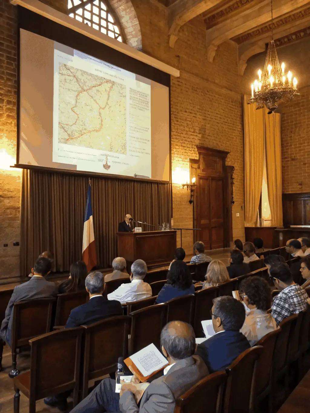 A picture of a group of adults attending a lecture on the architecture and history of the Château de Chantemille, held in one of the castle's halls.